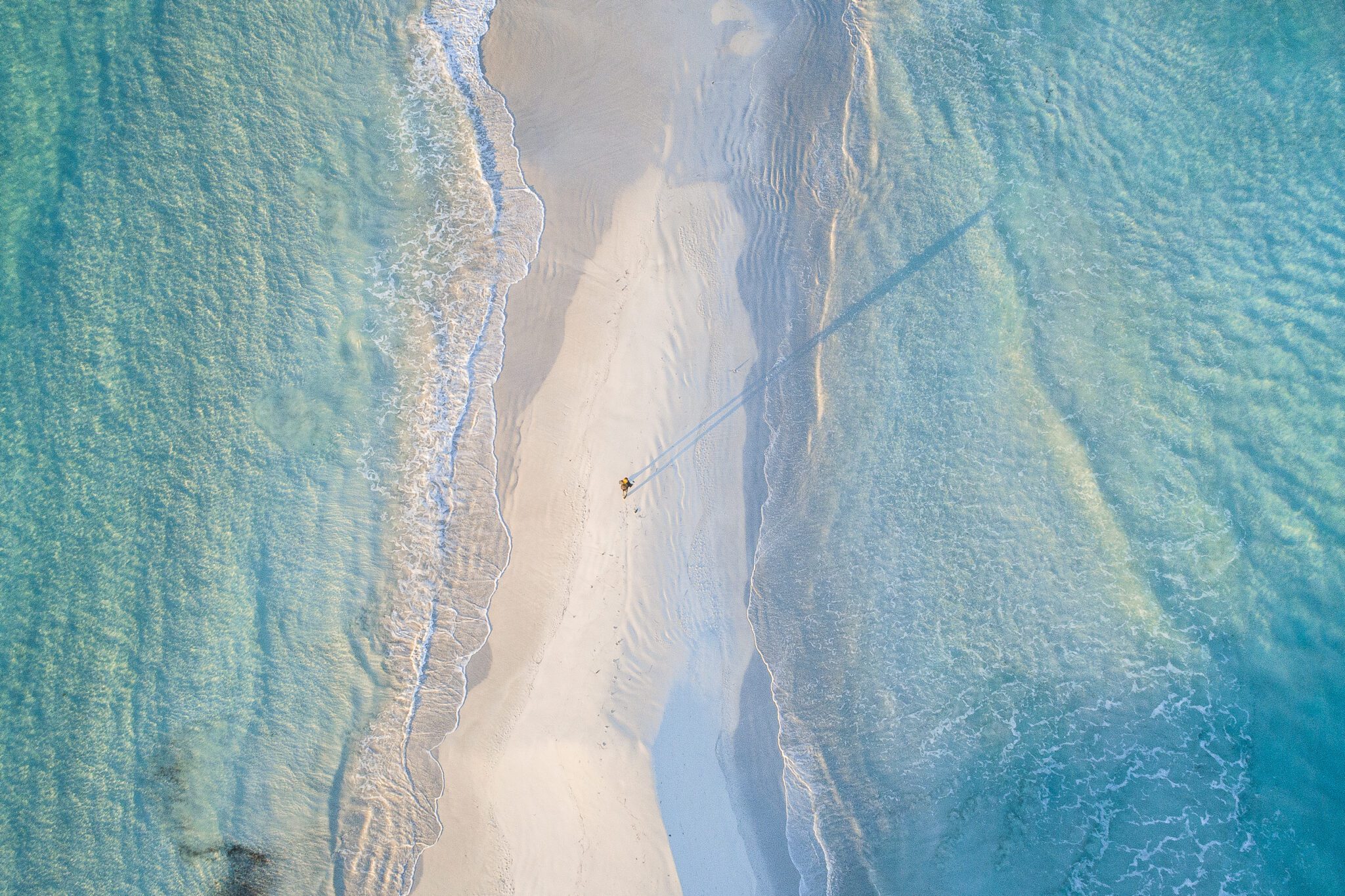 Aerial view of a narrow sandy beach between turquoise waters.