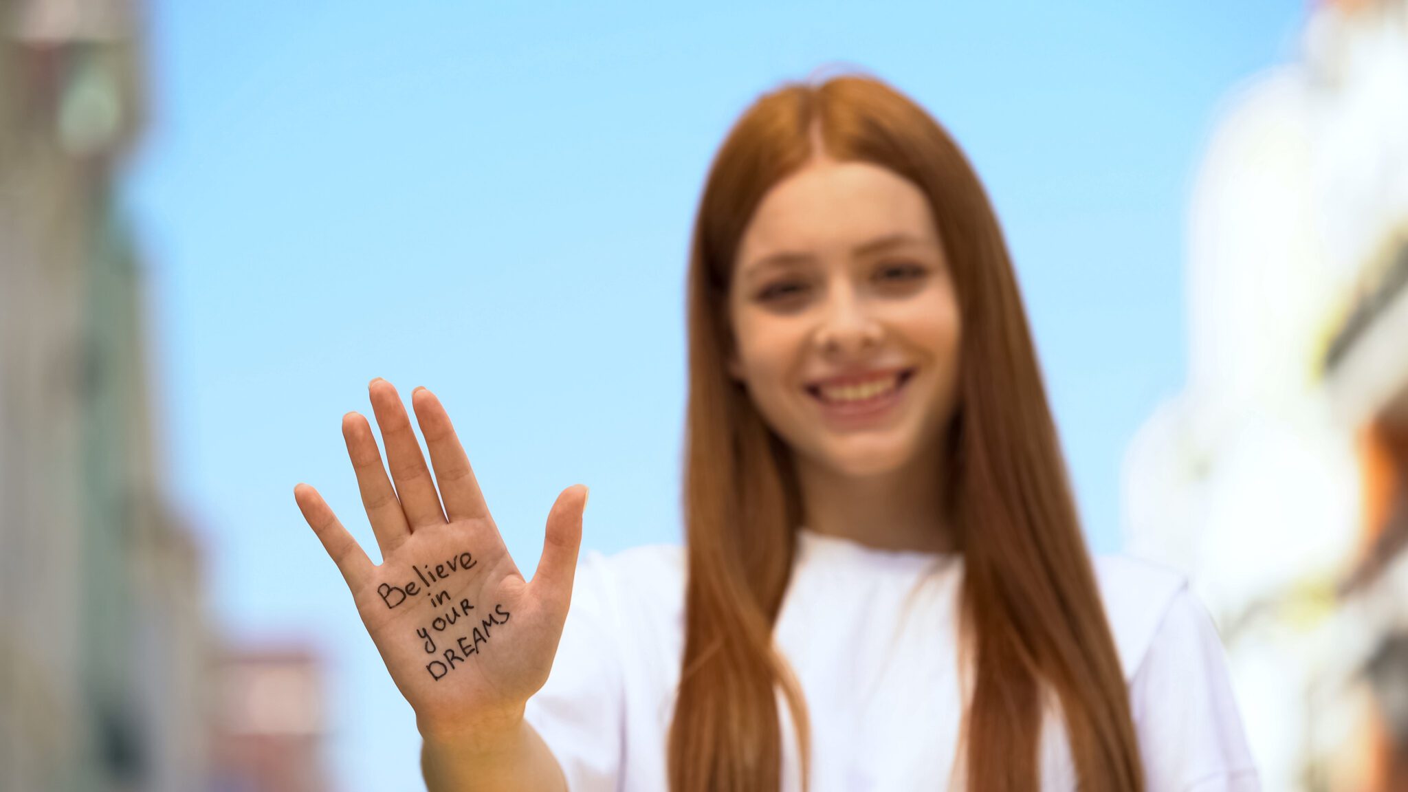 Smiling woman holds up hand with motivational message written on palm.