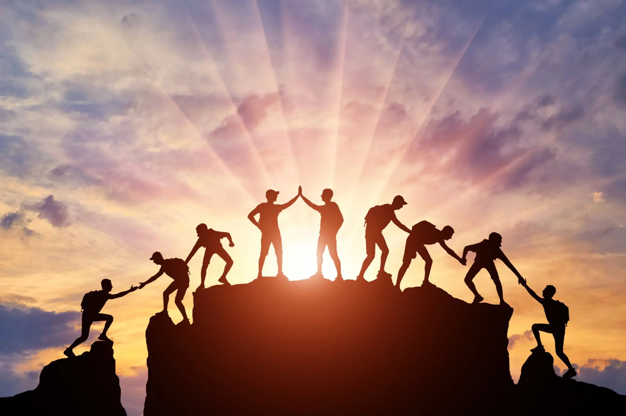 People helping each other climb a hill during a sunrise.