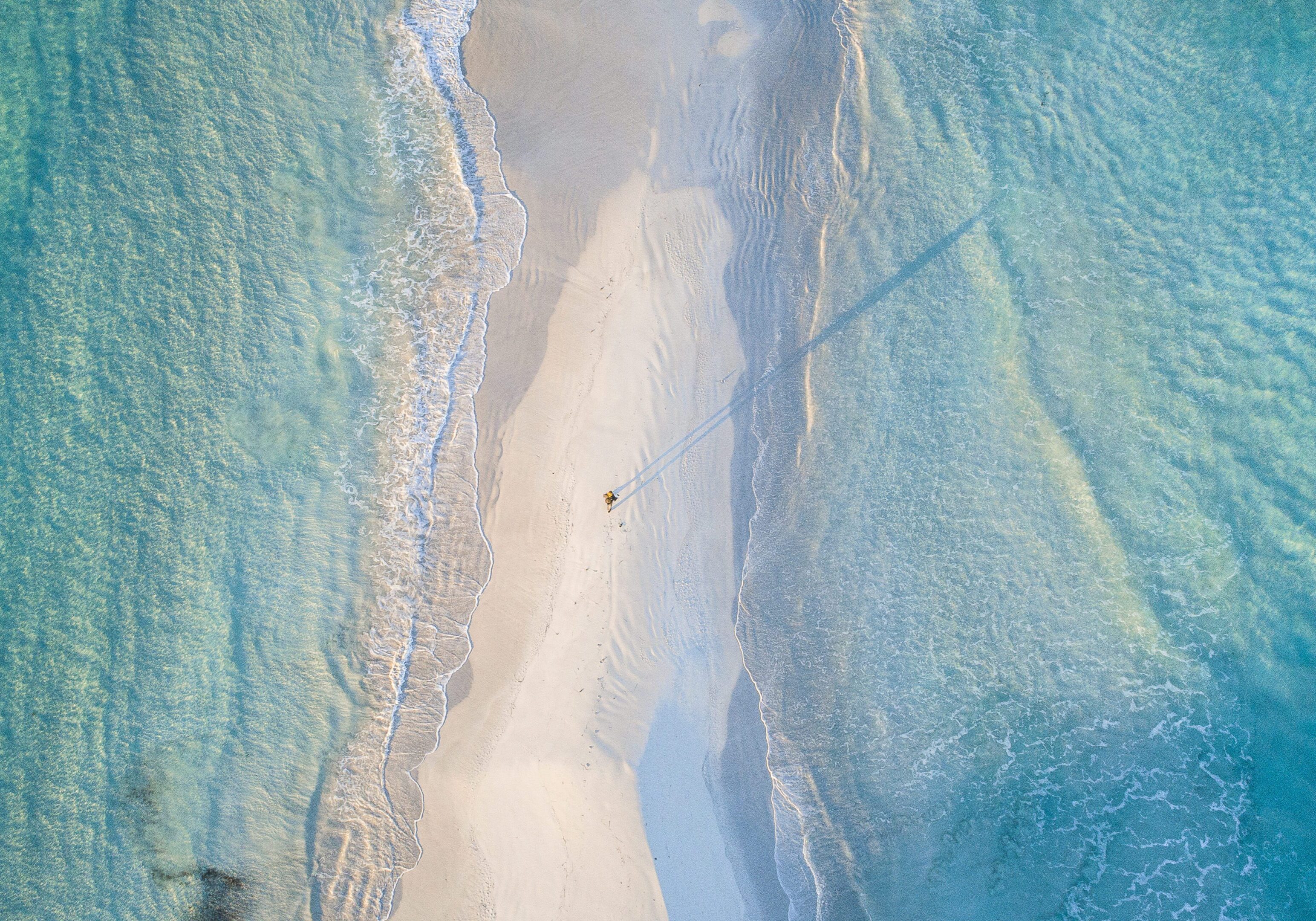 Aerial view of a narrow sandy beach between turquoise waters.