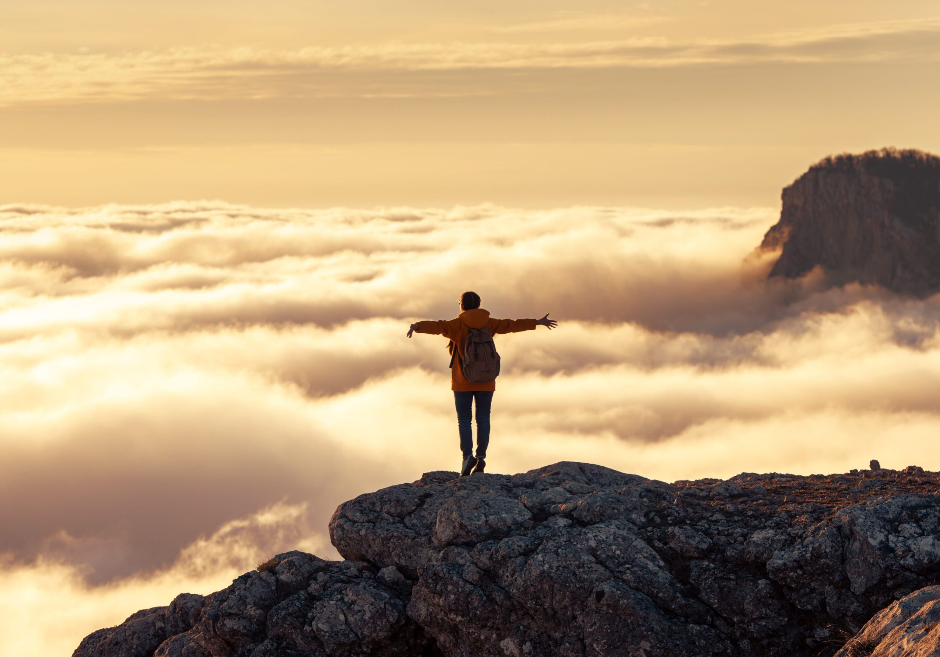 Person standing on a cliff above the clouds at sunrise.